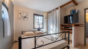 Ein Schlafzimmer mit Bett, Fernseher, Fenster mit Vorhängen, Nachttisch und Wandbild.