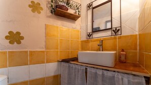 Ein Badezimmer mit einem weißen Waschbecken, gelb-weißen Fliesen, einem Spiegel und einem Ablagebereich mit Toilettenartikeln.