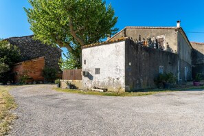 A rustic building with a gravel driveway, a large tree, and a brick wall. - Mon Petit Cabanon - Studio avec terrasse (Arles)