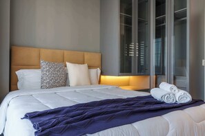 Ett hotellrum med en säng, kuddar, ett täcke och ett fönster med gardiner.