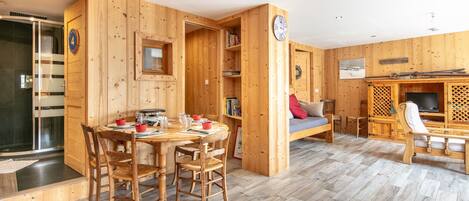 A wooden interior with a dining area, a sofa, a TV, and a bookshelf.