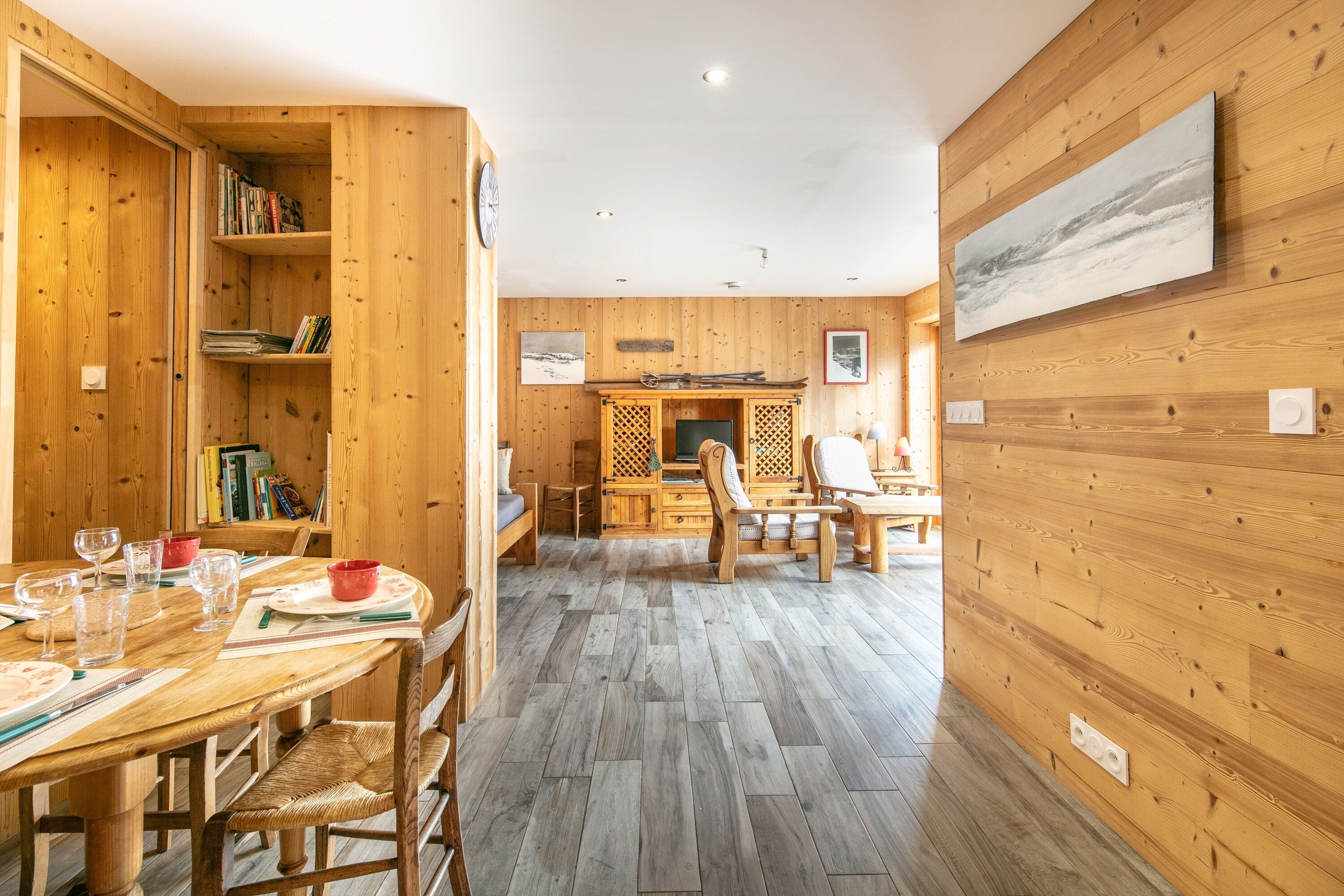 A wooden interior with a dining area, bookshelves, and a fireplace.