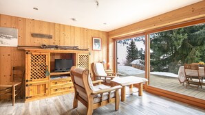 A wooden interior with a TV, seating, and a view of snow-covered trees. - Le Valhalla Chamrousse - Proche Télécabines (Chamrousse)