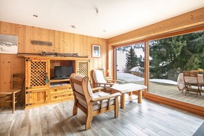 A wooden interior with a TV, seating, and a view of snow-covered trees. - Le Valhalla Chamrousse - Proche Télécabines (Chamrousse)