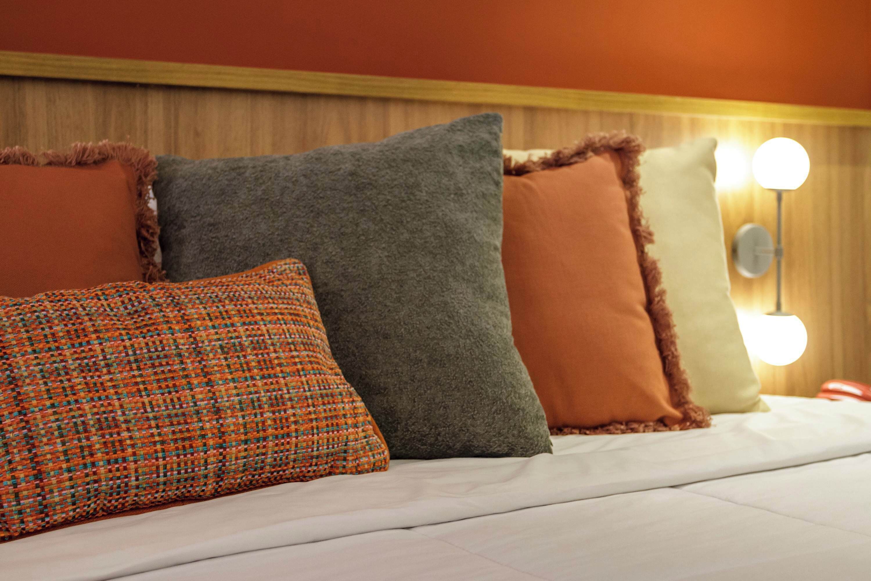 A bed with four pillows and a wall-mounted light fixture.