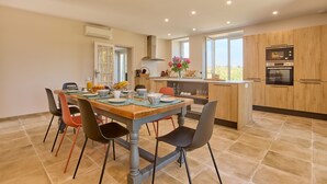 A modern kitchen with a central island, a dining table with chairs, and a view of the outdoors. - Gîte Le Séquoia de Saint Martin - Maison spacieuse (Seyches)