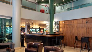 Eine moderne Lobby mit Barbereich, Ledersitzmöbeln und einer Glastrennwand, die auf die untere Ebene blickt.