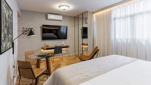 Ein Hotelzimmer mit Bett, Schreibtisch mit Stuhl, Fernseher und einem großen Fenster mit Vorhängen.