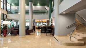 Eine großzügige Lobby mit einer zentralen Bar, verschiedenen Sitzgelegenheiten und einer Treppe.