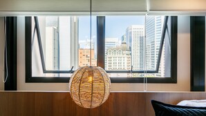 Ein Zimmer mit einem großen Fenster, einer gewobenen Leuchte und einem Bett mit einem schwarzen Kissen.
