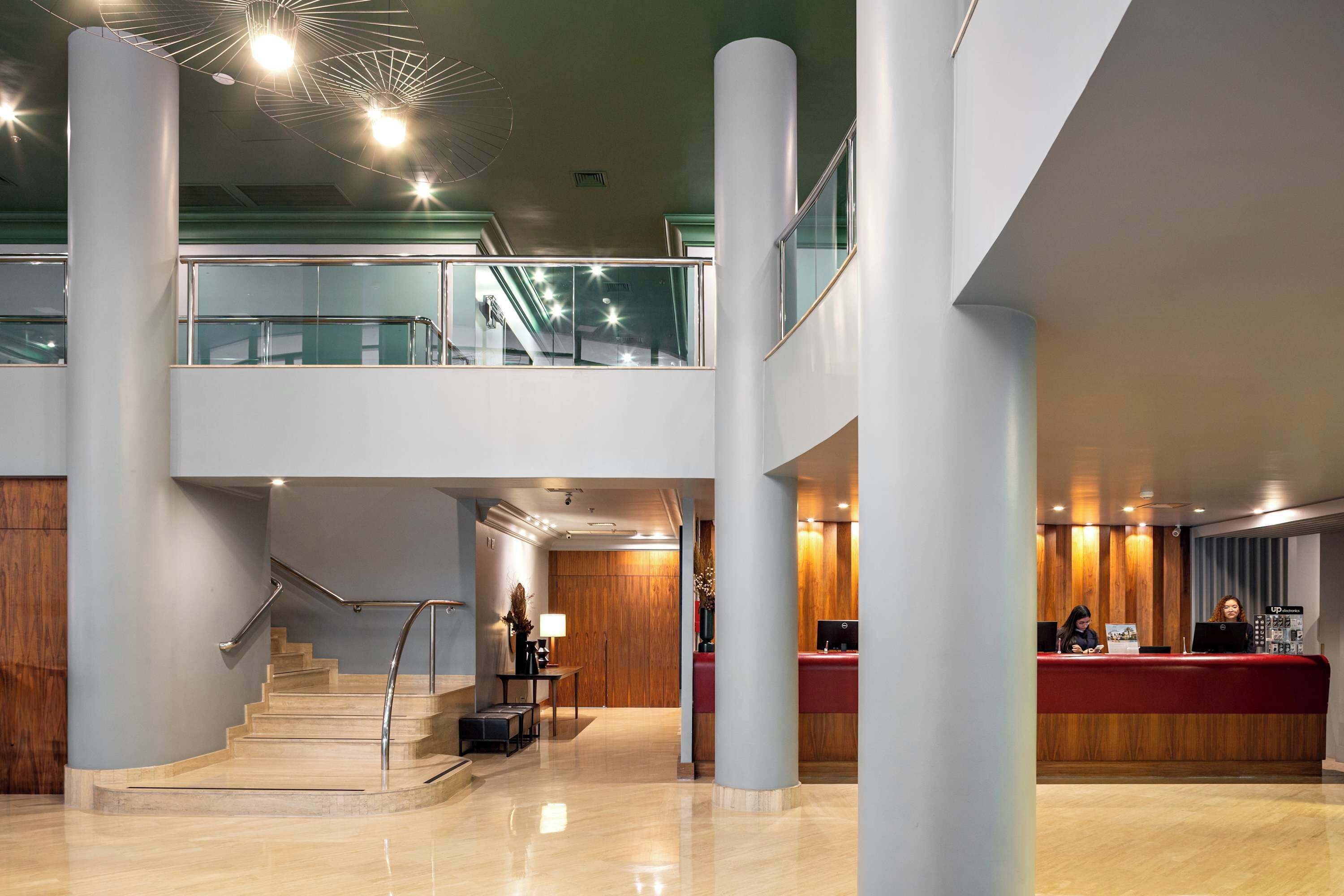 Een moderne hotellobby met een receptiebalie, een trap en een balkon op de tweede verdieping.
