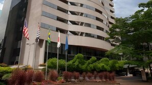 A tall, curved hotel building with multiple balconies, surrounded by greenery and flags. - #TB413 | Cyclinn Berrini Brooklin (Berrini)