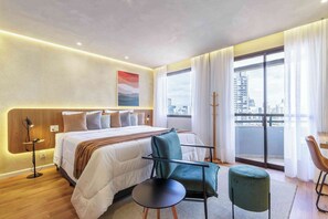 Habitación de hotel moderna con una cama grande, un escritorio, una silla y vistas a la ciudad.