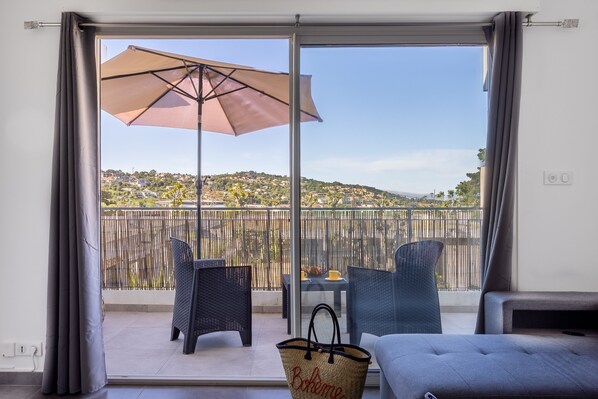 Ein Balkon mit Blick auf eine hügelige Landschaft, Korbstühle, ein Tisch und ein großer Sonnenschirm.