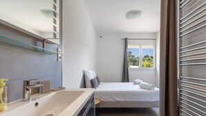 Habitación de hotel moderna con lavamanos grande en el baño, cama con vistas al exterior y cortinas en la ventana.