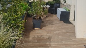 Un corridoio esterno stretto con piante in vaso, pavimento in legno e un piccolo tavolo con sedie.