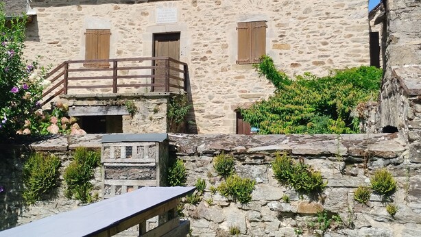 Un edificio in pietra con un balcone in legno, una piccola finestra e un cartello con del testo.