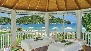 Een prieel met twee massagetafels, uitzicht op zee en een terras met parasols.