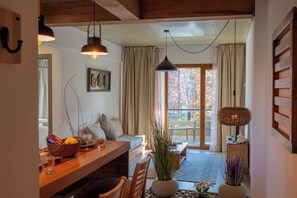 A cozy room with a wooden dining table, a sofa, and a large window with curtains. - Campichuelo Suit (San Carlos de Bariloche)