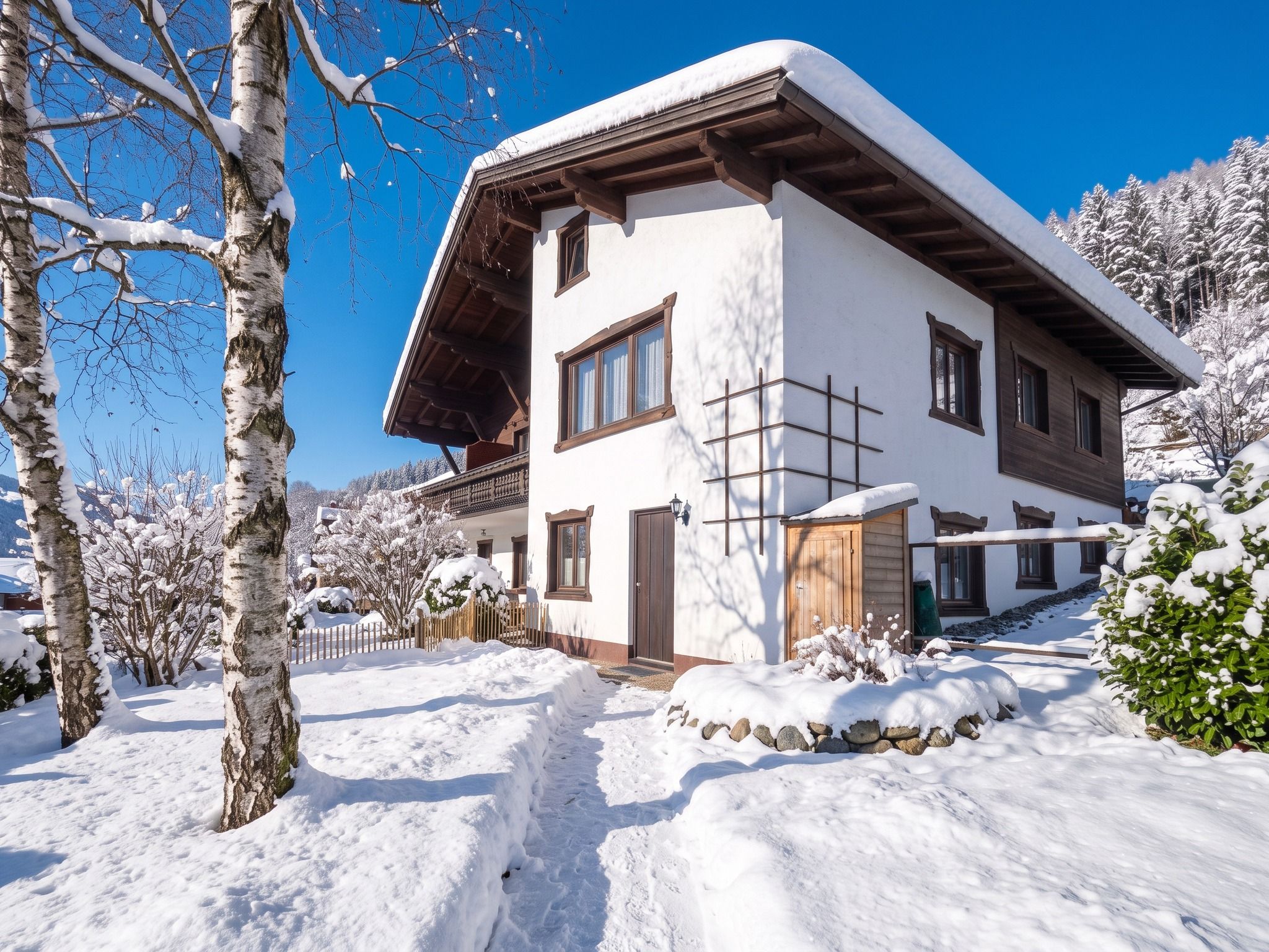 A two-story chalet with a sloped roof, wooden exterior, and a snow-covered landscape.