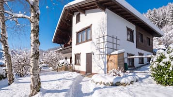 A two-story chalet with a sloped roof, wooden exterior, and a snow-covered landscape.