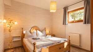 A wooden bed in a room with a 'WELCOME' sign, a radiator, and a window with curtains. - Relaxing break on the sunny slope with garden (Westendorf)