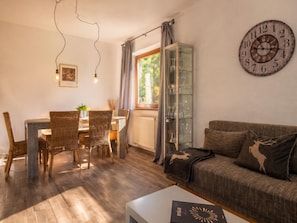A cozy living room with a dining area, a glass cabinet with glasses, a clock on the wall, and a sofa with a deer pillow. - Relaxing break on the sunny slope with garden (Westendorf)