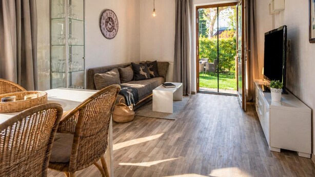 A modern living room with a sofa, a dining area with wicker chairs, a glass cabinet, a television, and a sliding glass door leading to a garden. - Relaxing break on the sunny slope with garden (Westendorf)