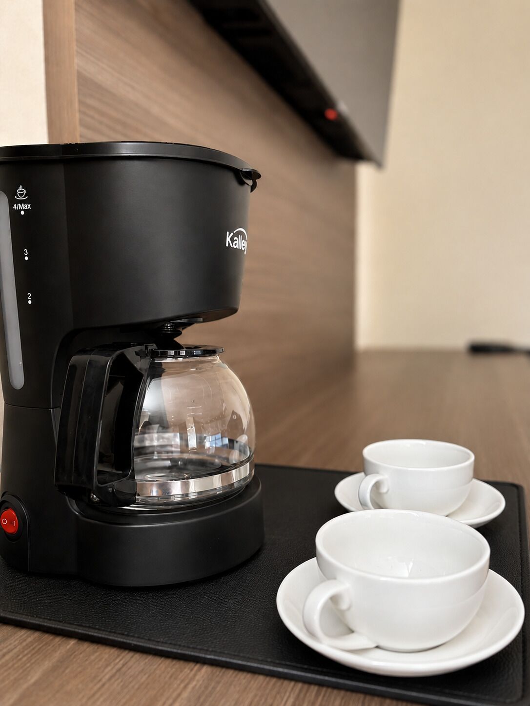 A black coffee maker with a glass carafe and two white cups on a black tray.