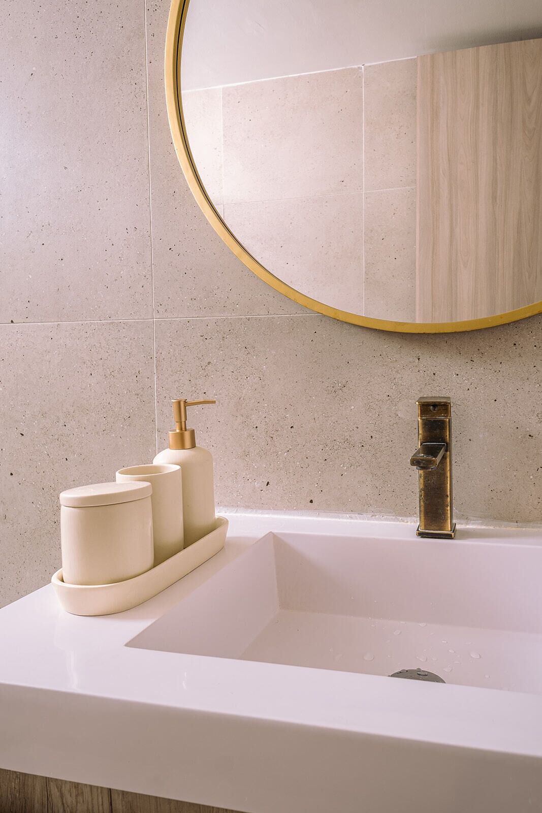 Ein Badezimmer mit einem weißen Waschbecken, goldenen Wasserhähnen und einem runden Spiegel mit goldener Rahmung.