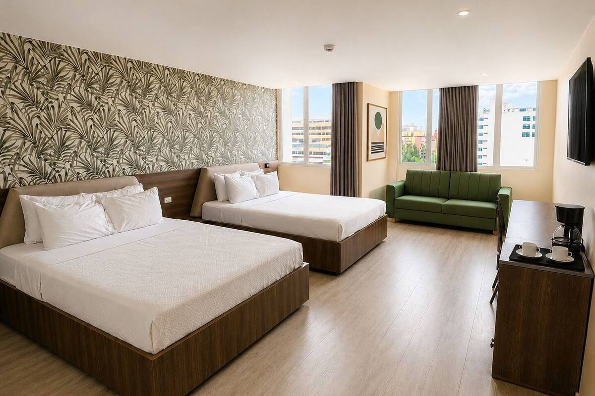 A hotel room with two beds, a green sofa, a coffee station, and a city view.