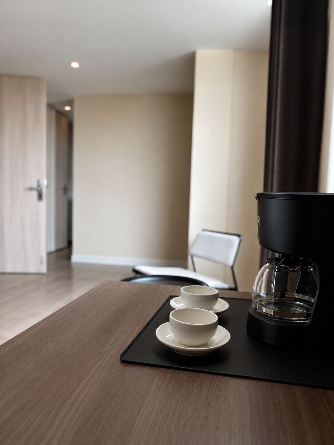 A hotel room with a wooden table, a coffee maker, and two cups on a black coaster.