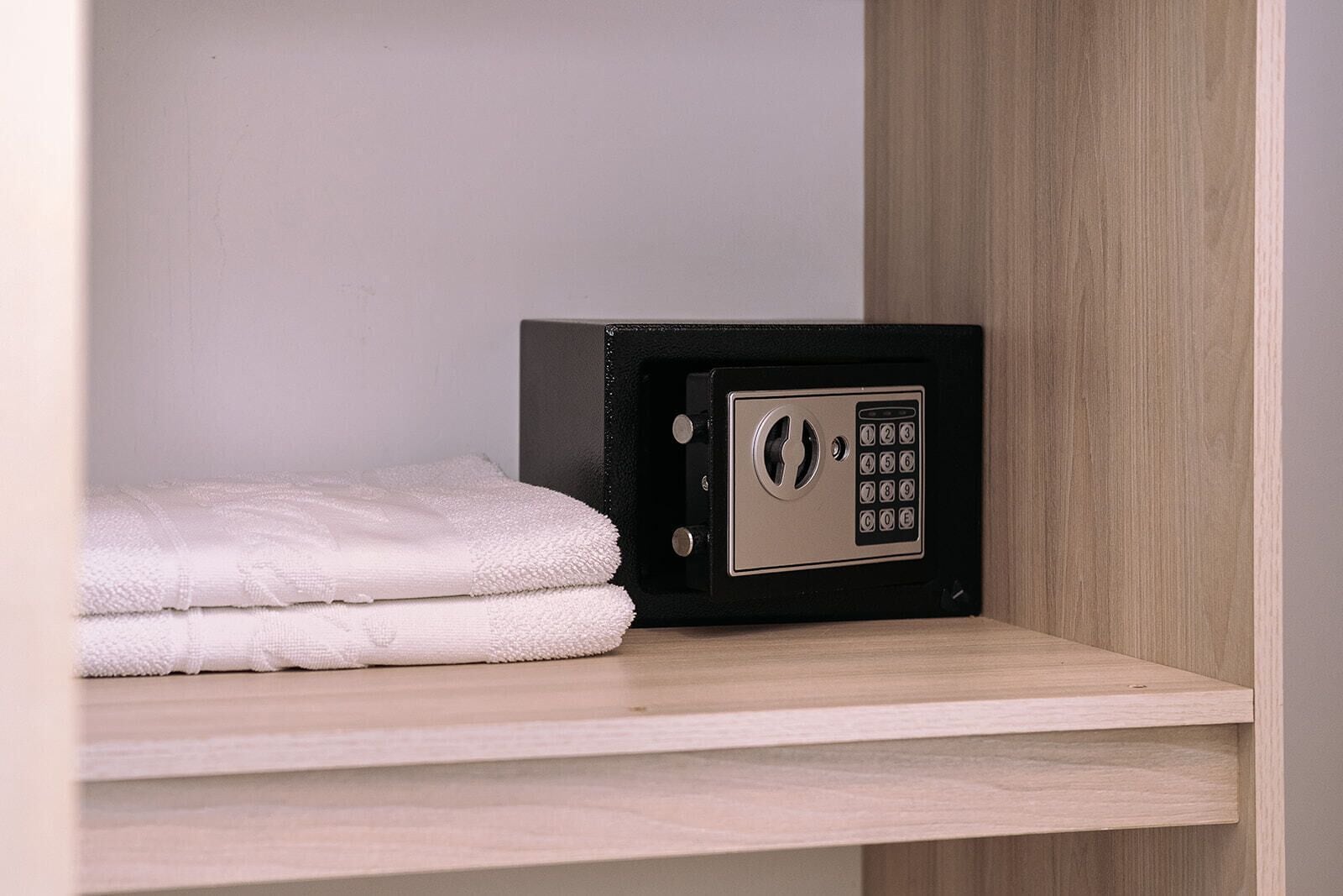 A safe deposit box with a keypad lock and a folded white towel on a wooden shelf.