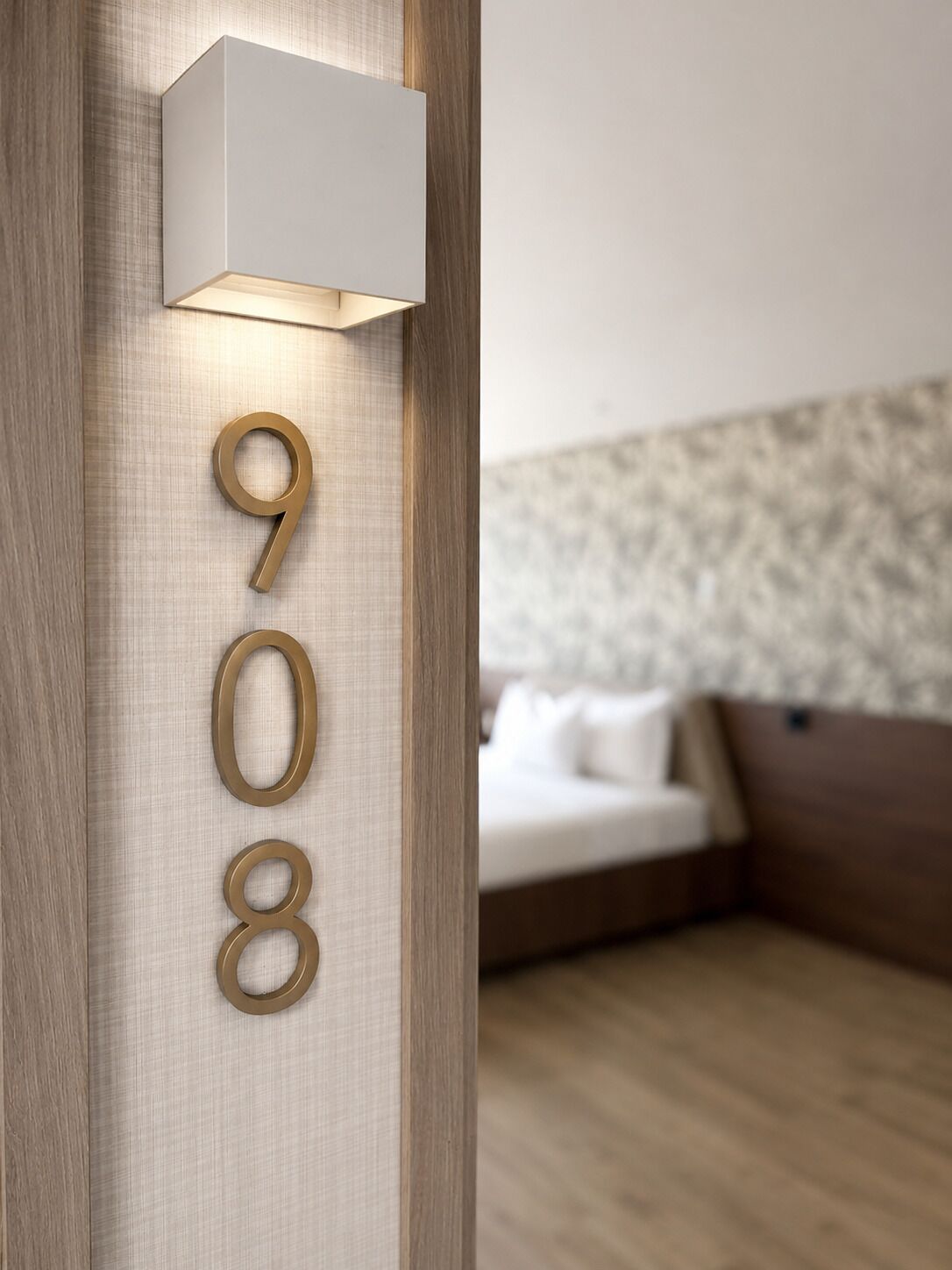 Una habitación moderna con piso de madera, cama con ropa de cama blanca y una lámpara de pared que muestra el número 908.