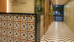 Un'area di accoglienza hotel con pavimento a motivi geometrici, una reception con un logo e una lampada a sospensione.