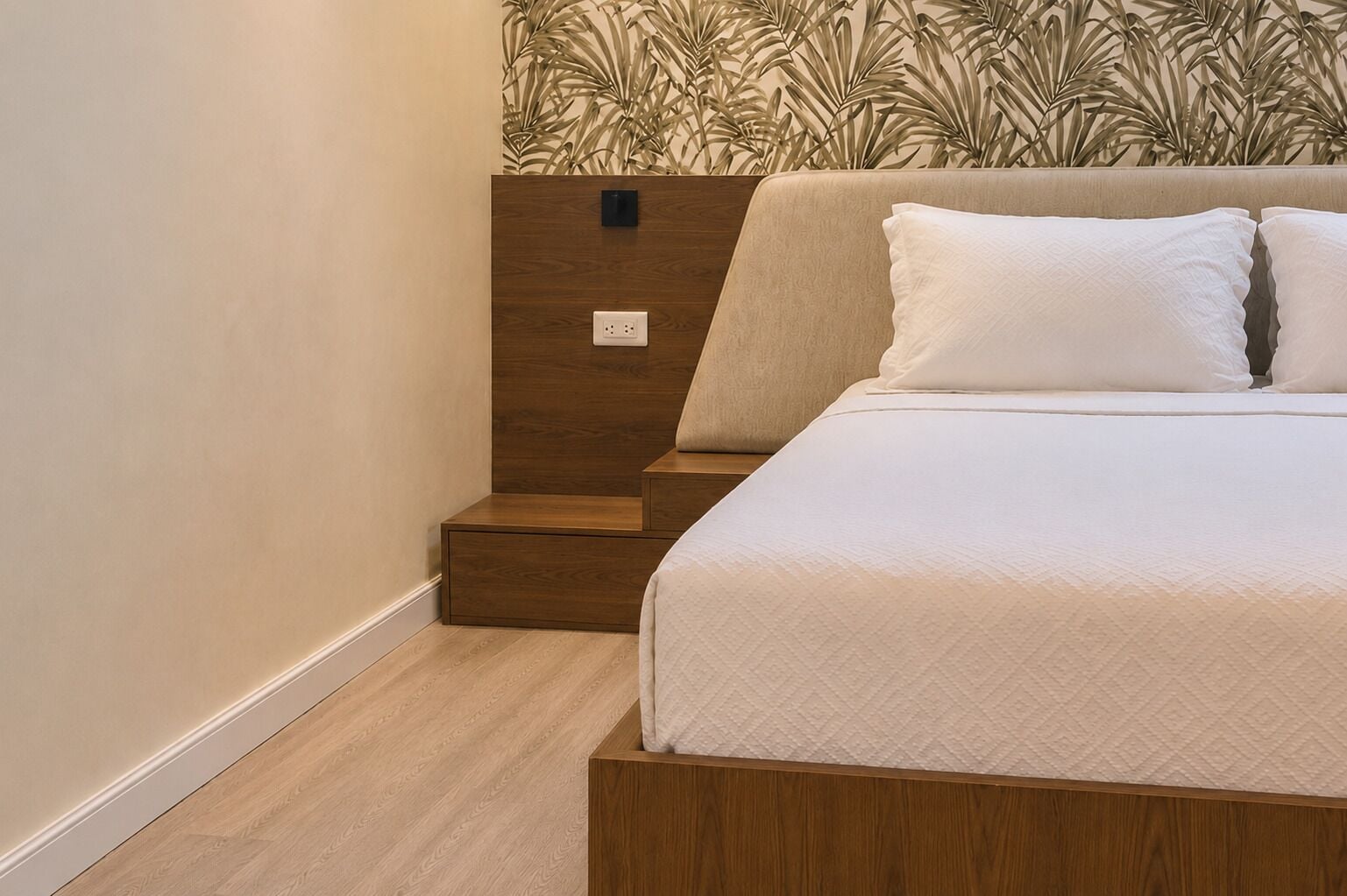Un dormitorio con una cama, una mesita de noche, un enchufe y una pared con un diseño de hojas.