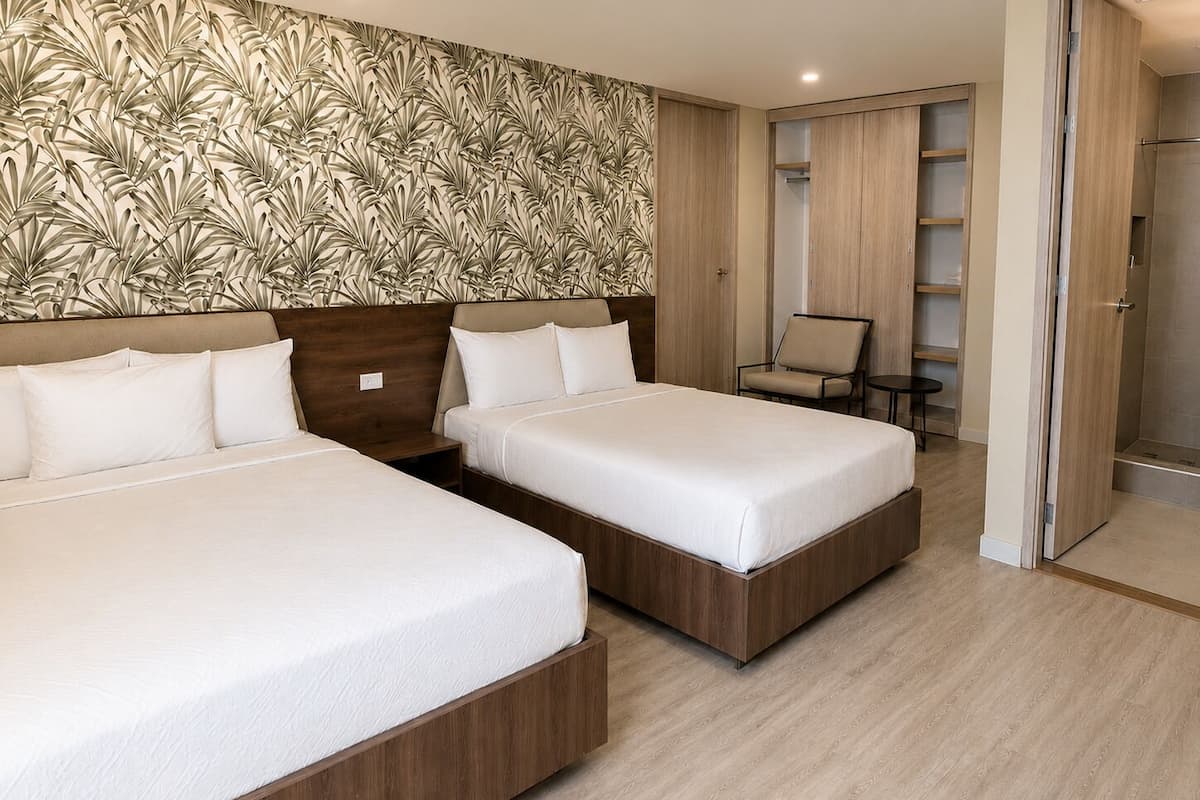 A hotel room with two beds, a wooden headboard, a patterned wall, a chair, and a walk-in closet.