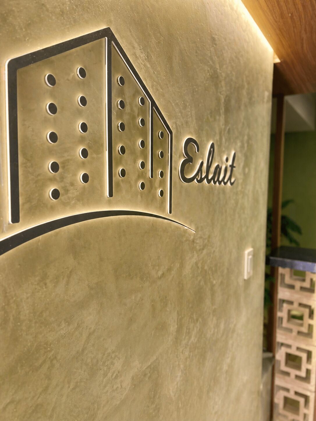 Un mur à la texture particulière, orné du contour d’un bâtiment et du mot « Estait » écrit en lettres cursives.