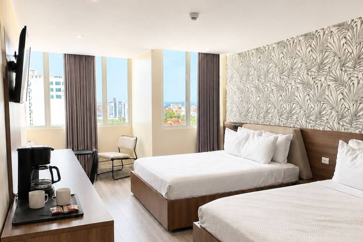 A hotel room with two beds, a desk with a coffee maker, and a view of buildings.