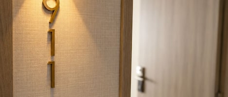 A wall-mounted light fixture with a number '9' and '1' on a textured wall, a wooden door in the background, and a door handle.