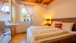 A bedroom with a wooden headboard, a bed with white bedding, a bedside lamp, and a window with curtains. - Lovely chalet with a large garden and terraces (Kötschach-Mauthen)
