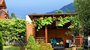 A wooden building with a covered porch, a small garden with various plants, and a mountain in the background. - Lovely chalet with a large garden and terraces (Kötschach-Mauthen)