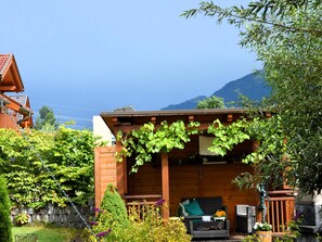 Un bâtiment en bois doté d’un porche abrité, d’un petit jardin avec différentes plantes et, au loin, d’une montagne.