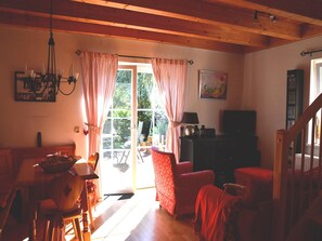 Una habitación acogedora con techo de madera, una mesa de comedor con sillas, un sofá, un televisor y una estantería.