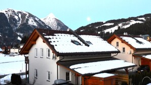 A residential area with snow-covered roofs, a parked car, and mountains in the background. - Lovely chalet with a large garden and terraces (Kötschach-Mauthen)