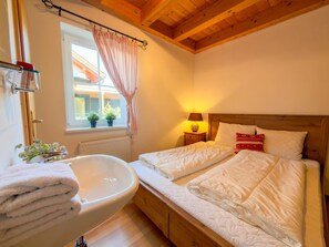 A bedroom with a wooden ceiling, a window with curtains, a bedside table with a lamp, and a bed with pillows. - Lovely chalet with a large garden and terraces (Kötschach-Mauthen)