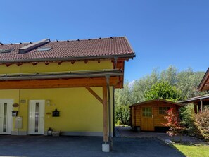 Een geel gebouw met een rode dakbedekking, een overdekte veranda en een kleine houten constructie op de achtergrond.