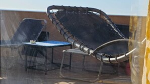 Un espacio al aire libre iluminado por el sol, con sillas de metal y una terraza de madera.