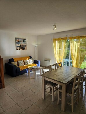Ein Wohnzimmer mit einer Couch, einem Esstisch, Stühlen, einer Lampe und einem Fenster mit Vorhängen.