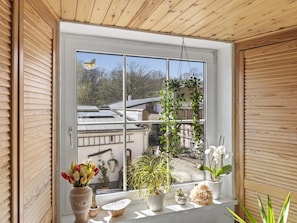 Ein Fenster mit Blick auf einen Garten, eine hängende Pflanze und eine Vase mit Blumen.